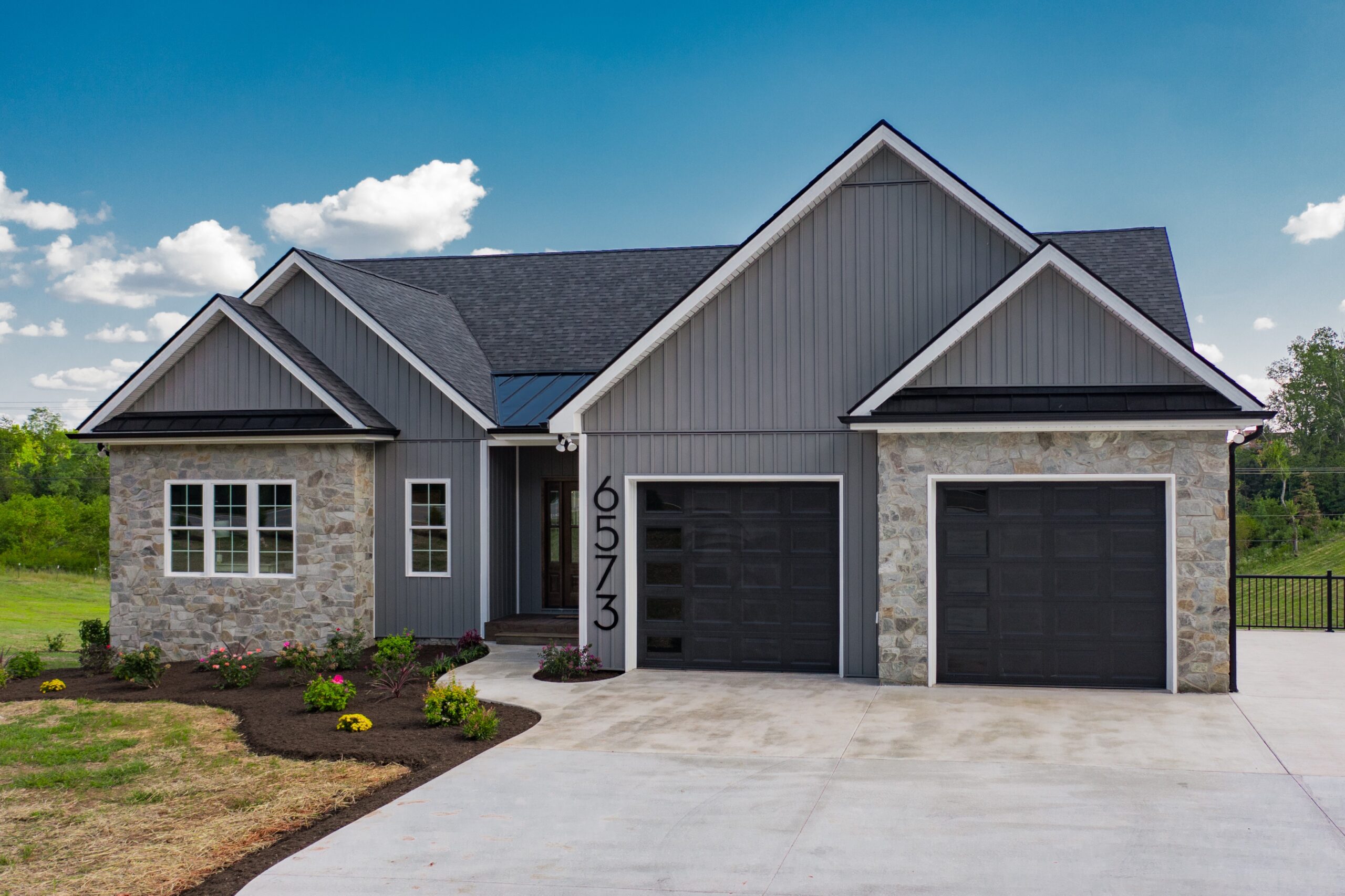 Blue gray home with black accents, accent garage doors that are black with windows running down the left side vertically, and accents of natural stone.