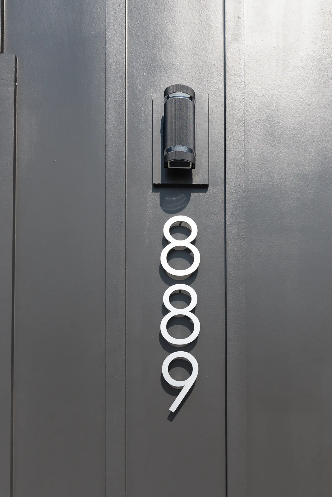 Modern house number 889 and wall light on dark siding of the LynBrook Home