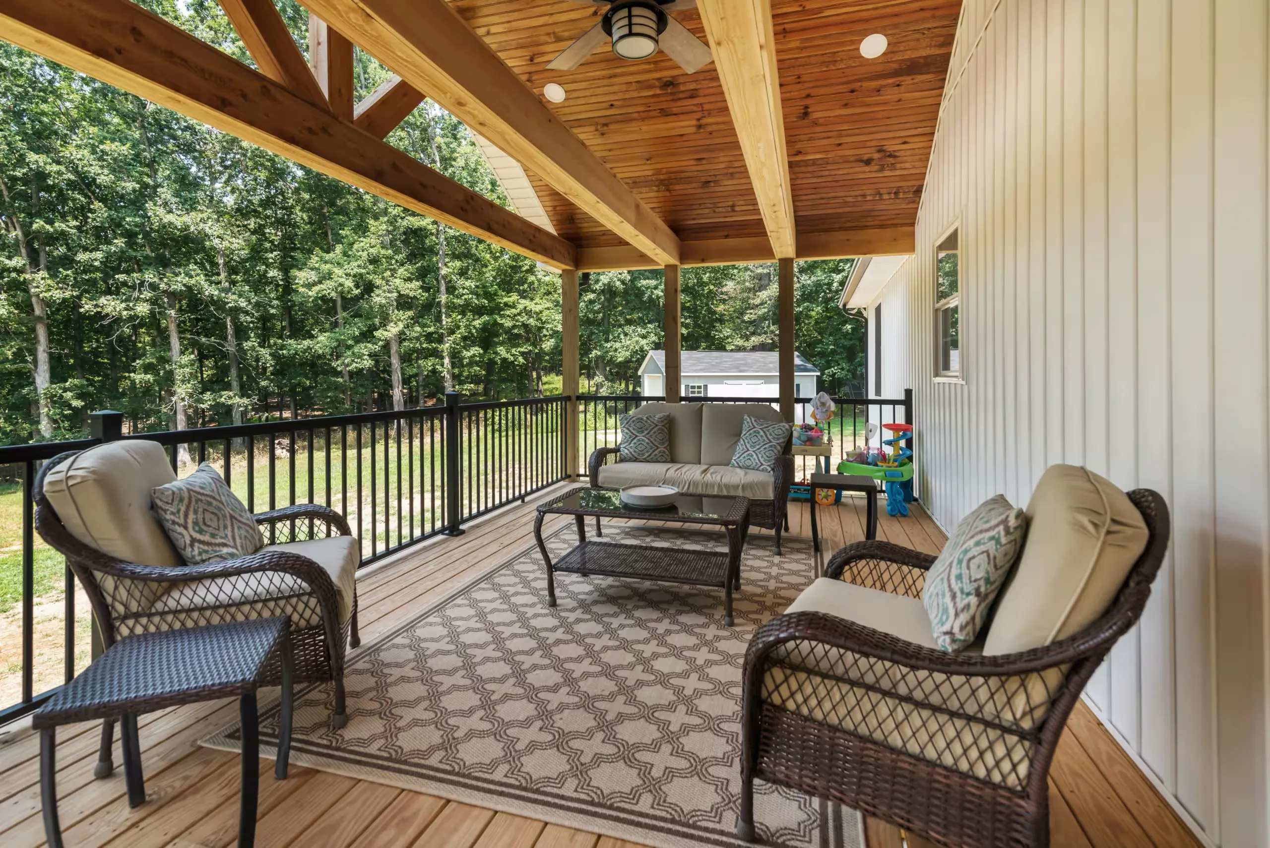 Covered rear deck with timber beams and outdoor seating at the Lake Cross Home
