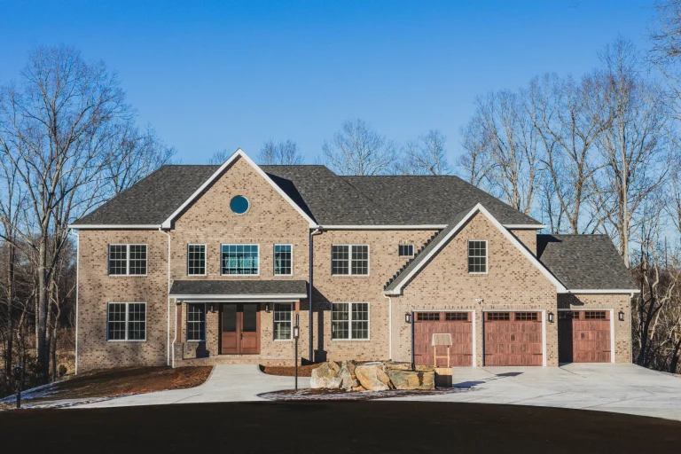 The exterior view of a spacious 7463 square foot brown brick mansion with a large concrete driveway and beautiful wooden garage doors.