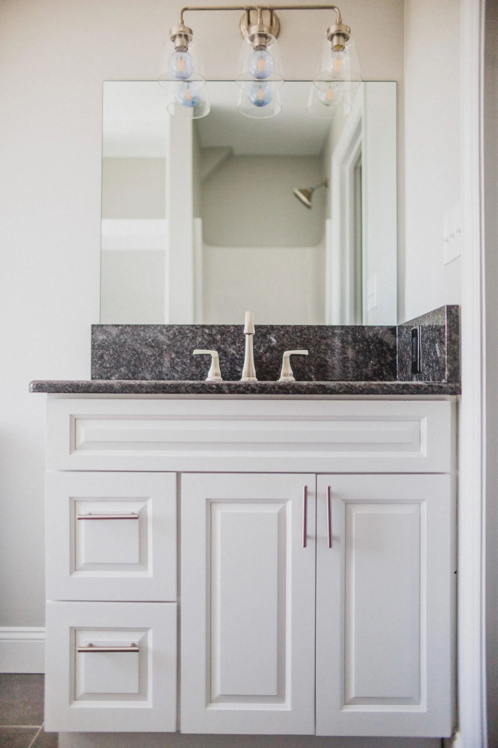 White bathroom vanity with granite top and three-light fixture in the Falling Creek Home