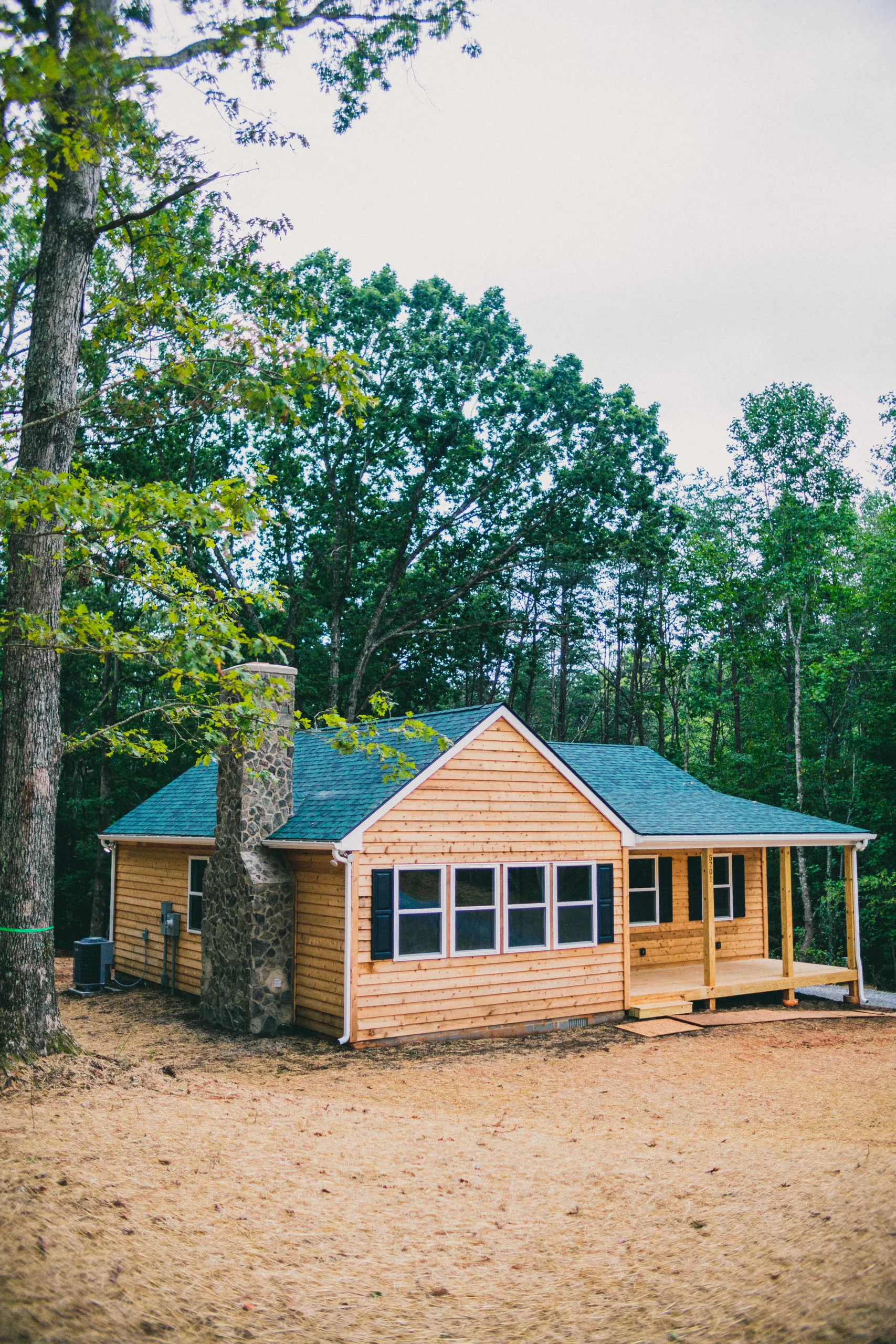 Side view of the Forest Home with stone chimney and covered porch among trees