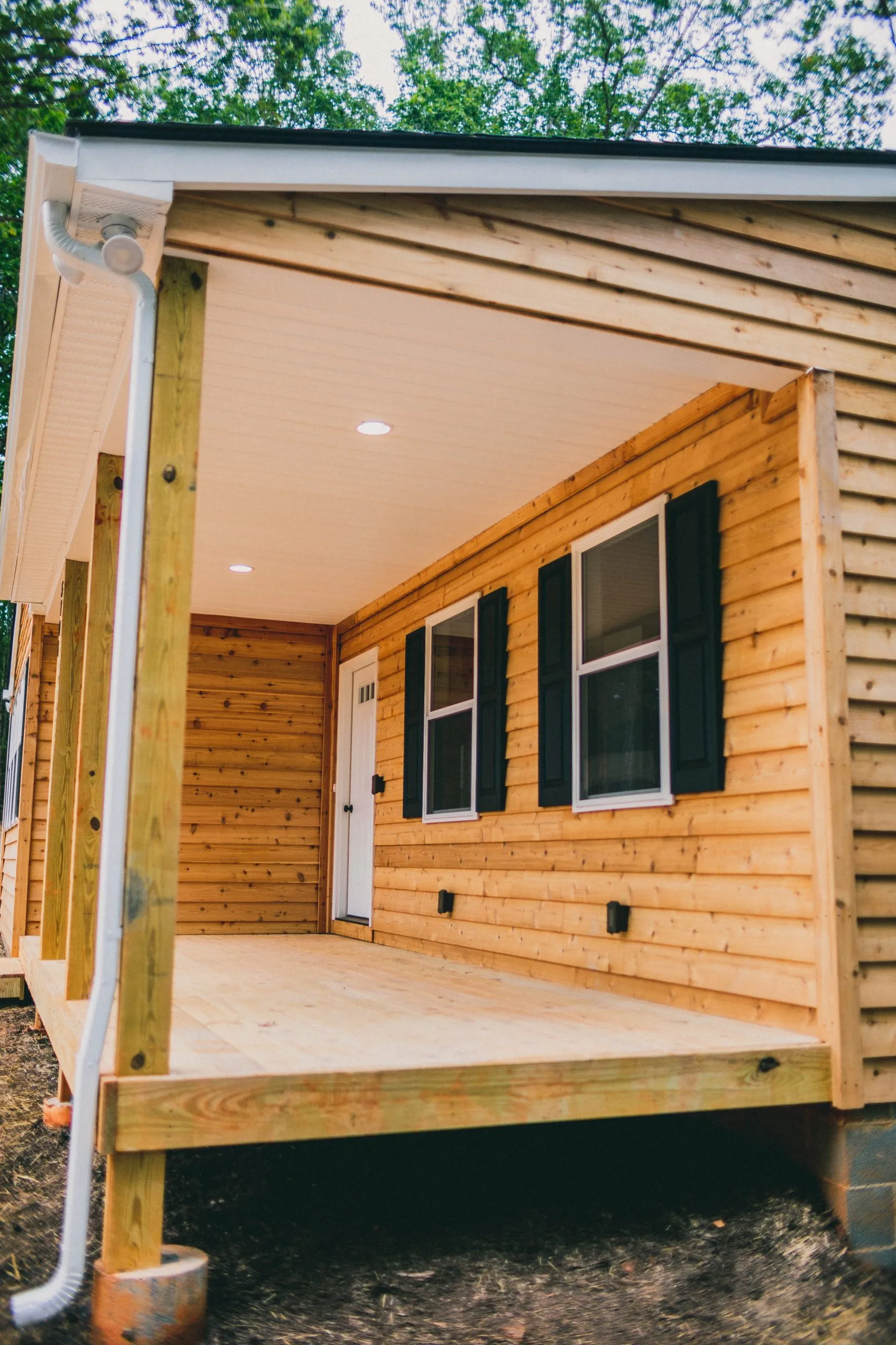 Covered front deck with cedar siding and black shutters on the Forest Home