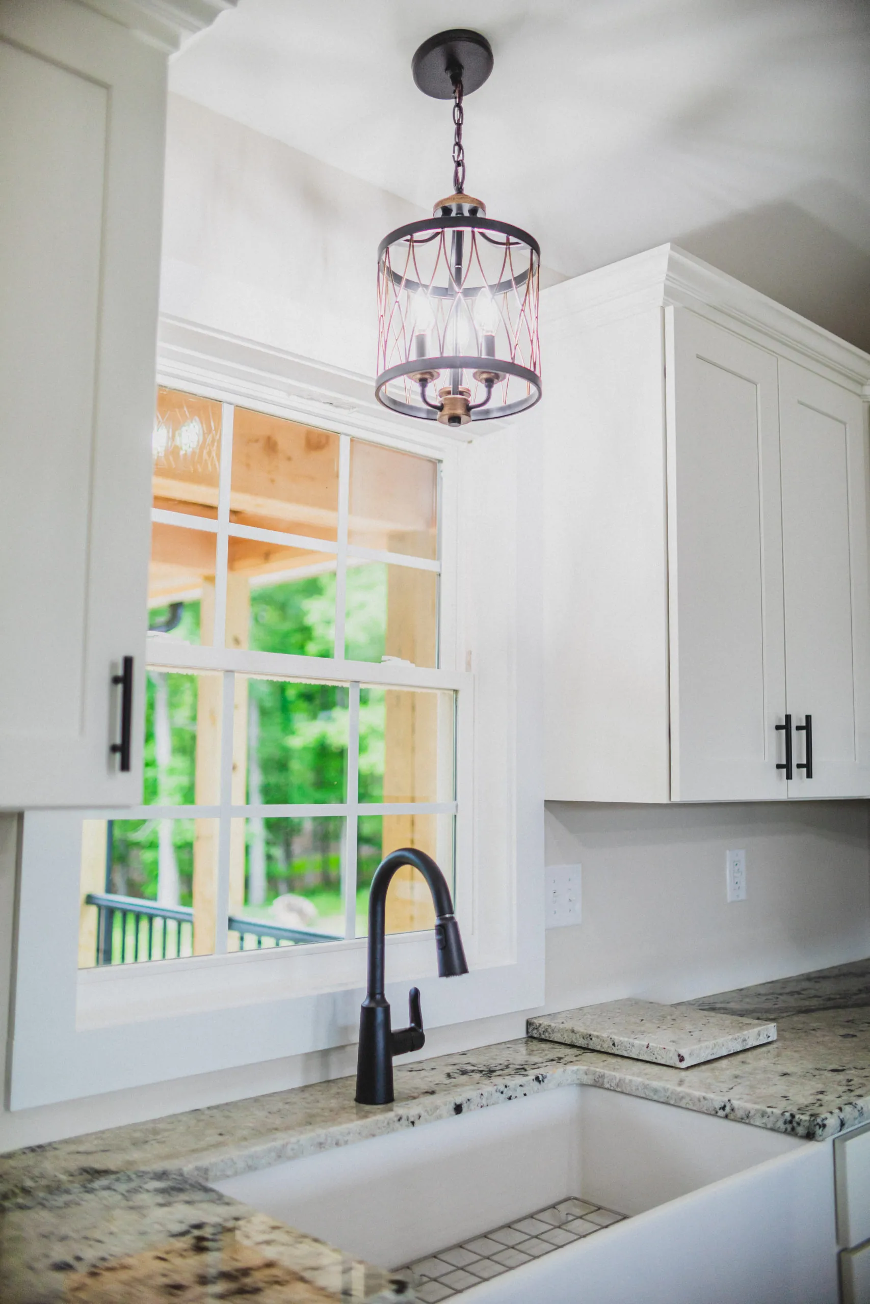 Kitchen sink with black faucet and pendant light under a window in the Lake Cross Home