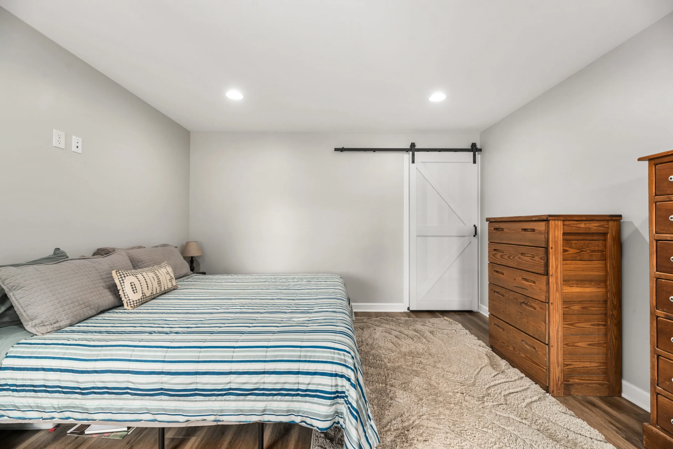 Primary bedroom with white barn door and wood dresser in the Timber Ridge Home