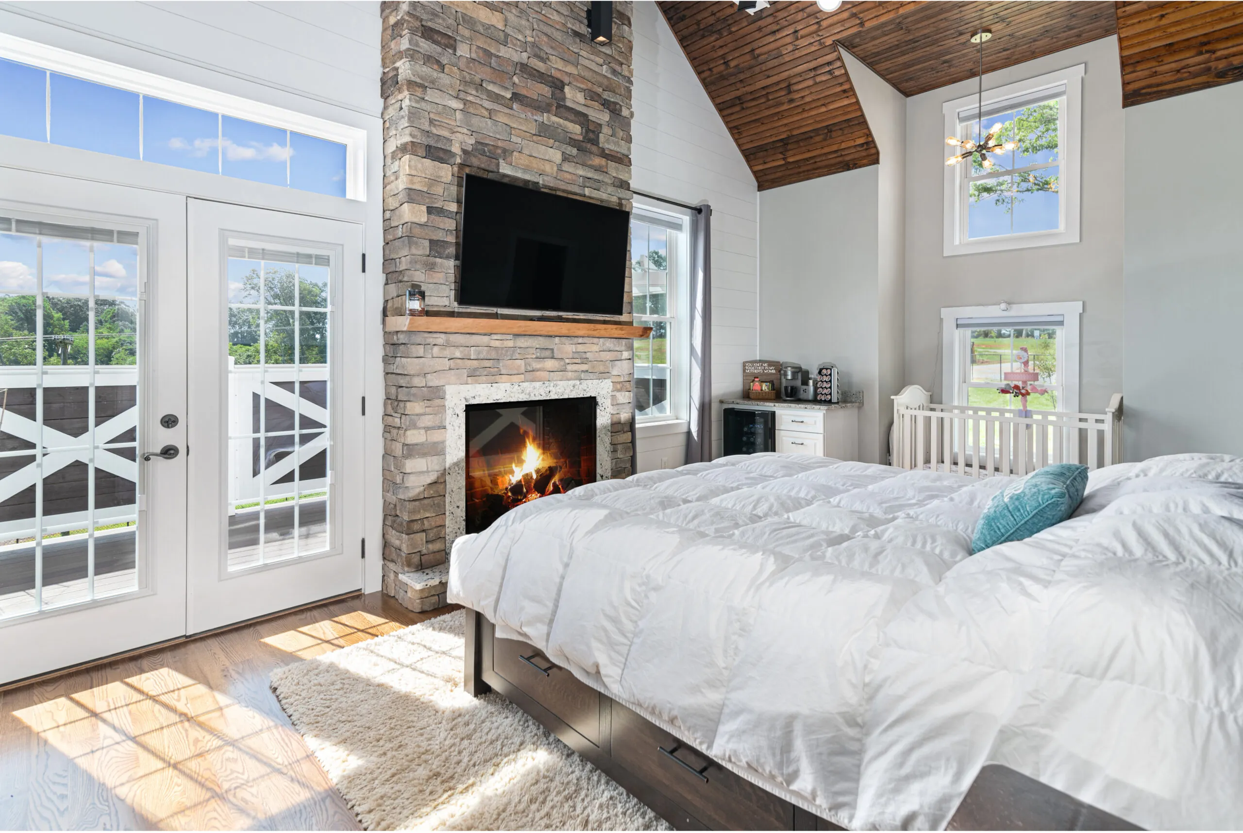 Primary bedroom with stone fireplace and vaulted wood ceiling in the Lowry Home