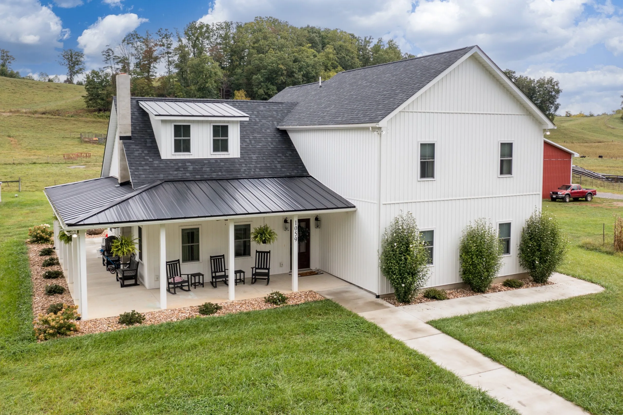 White farmhouse style home with black metal roof accent and black front door. Beautiful landscaping using river rock and green bushes surrounds the home.