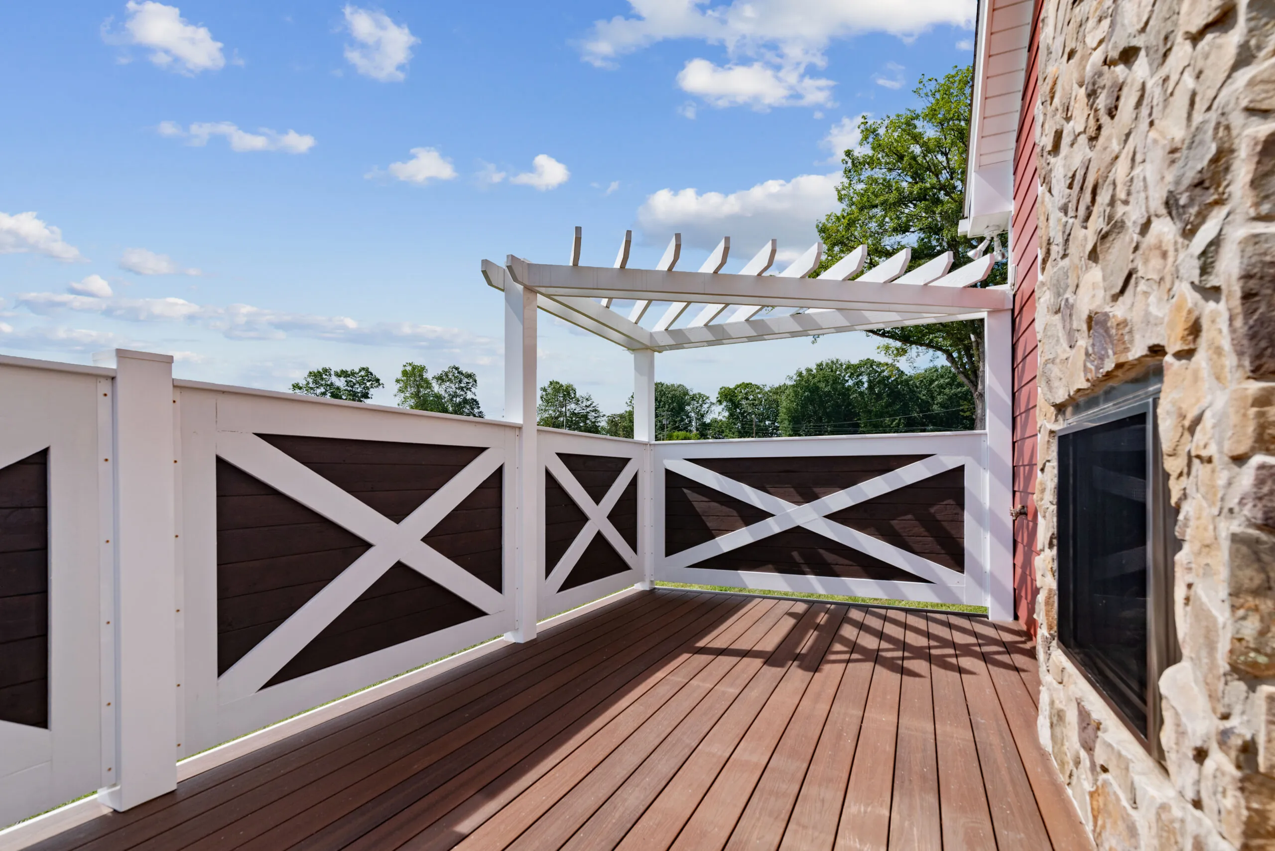 Deck with white and brown X-pattern railing and pergola at the Lowry Home