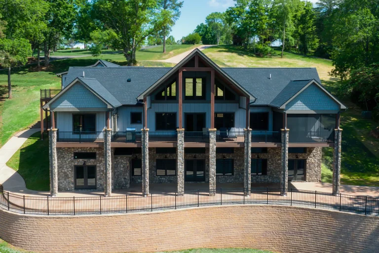 Lake-facing back of the Waterford Home with stone columns, blue siding and a walkout terrace