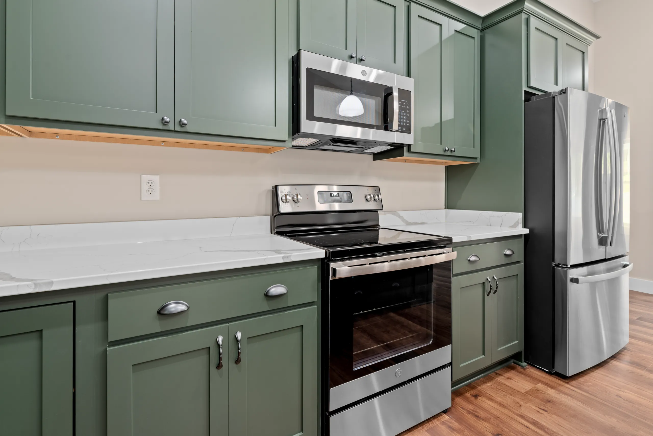 Stainless range, microwave and refrigerator with green cabinets in the Lake Crest Home