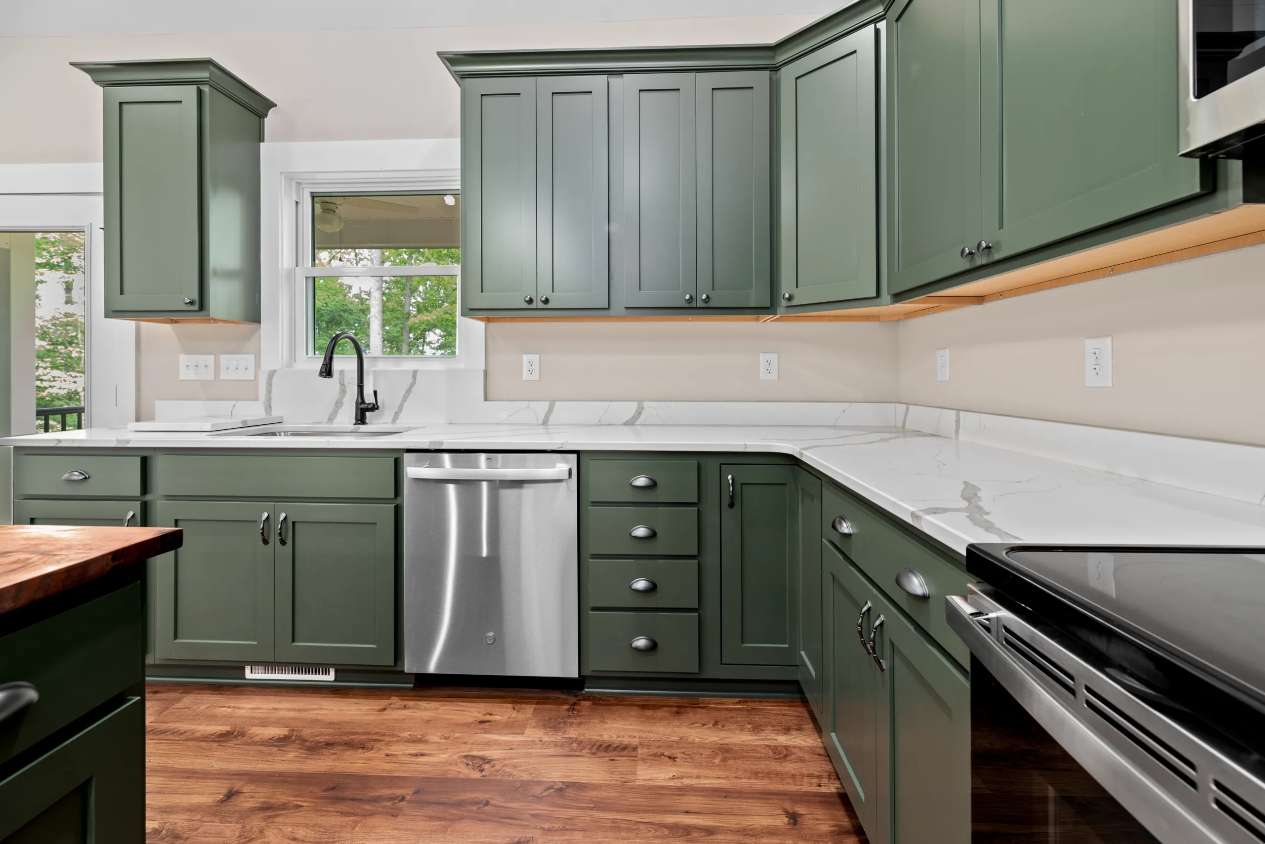 Green kitchen cabinets, stainless dishwasher and quartz counters in the Lake Crest Home