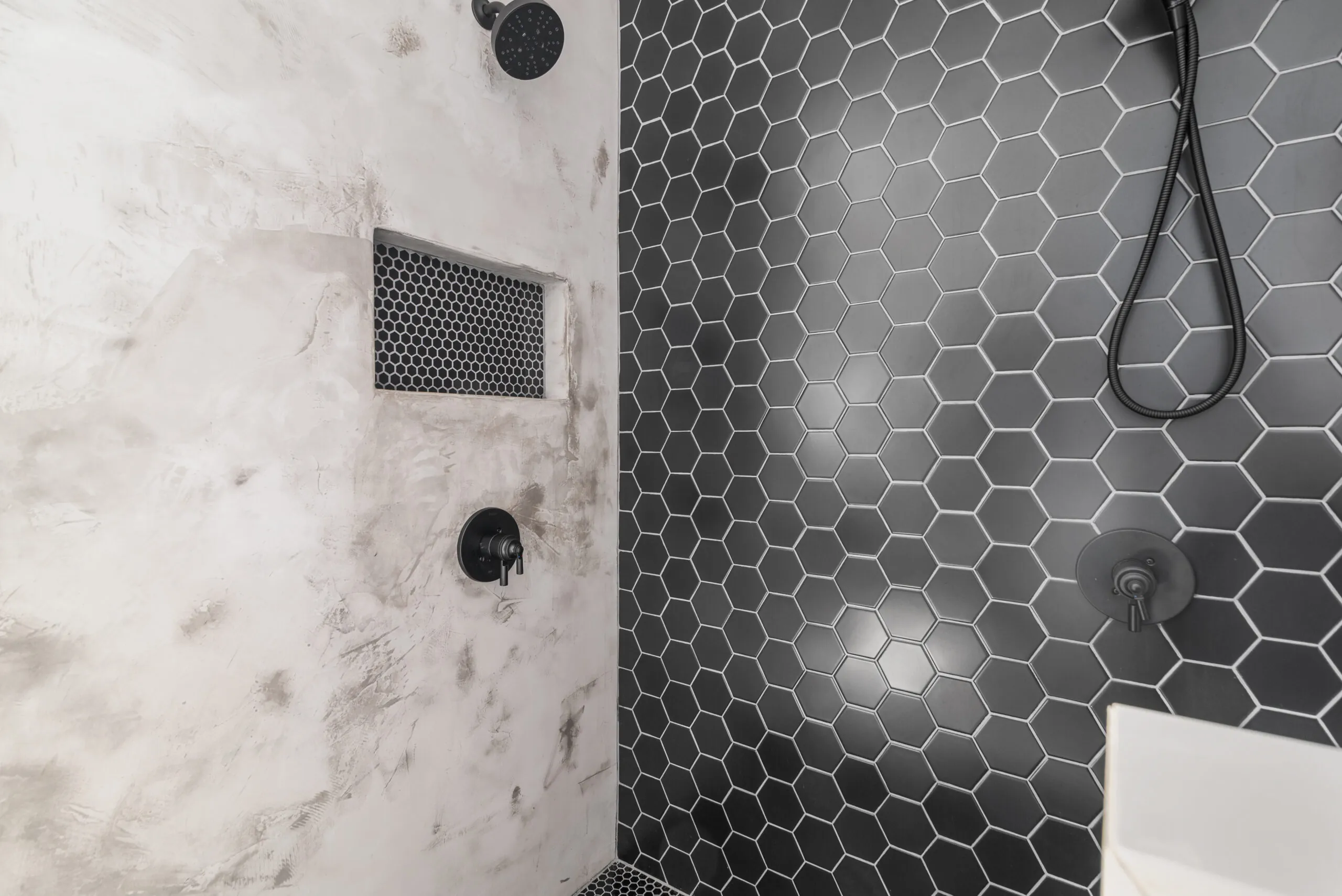 Shower detail with black hex tile, plaster-look wall and niche in the LynBrook Home