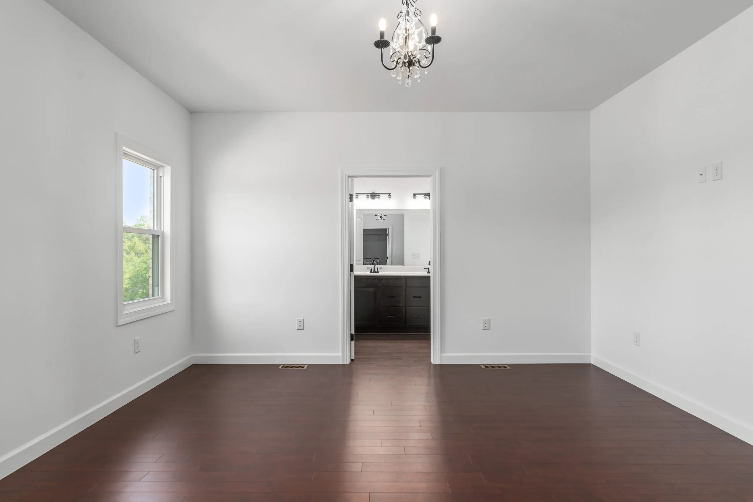 Empty bedroom with chandelier and view into the bathroom in the Otterlea Home