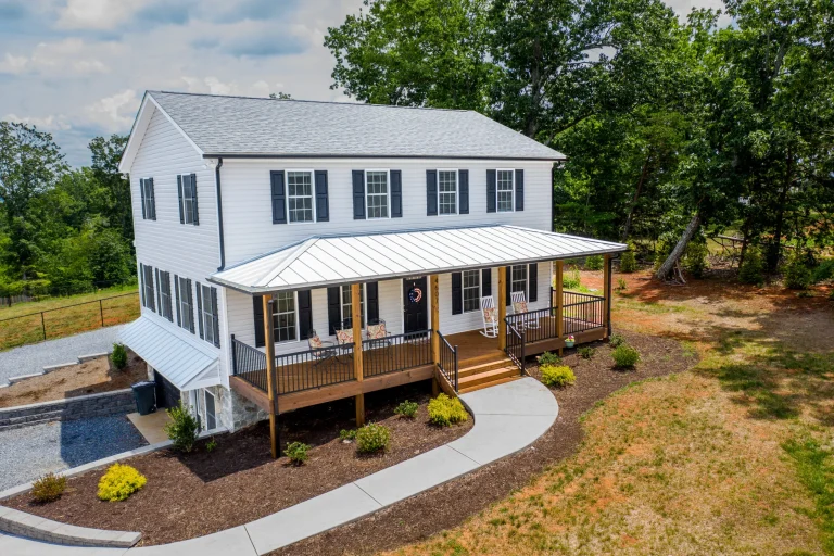 Exterior of the Timber Ridge Home, a two-story white house with a metal-roof wraparound porch and black shutters