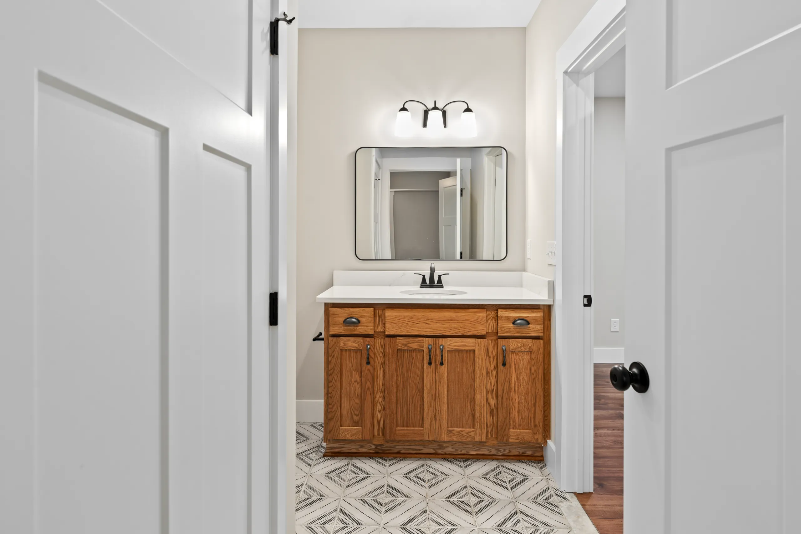 Oak vanity with black-framed mirror and patterned tile floor in the Lake Crest Home