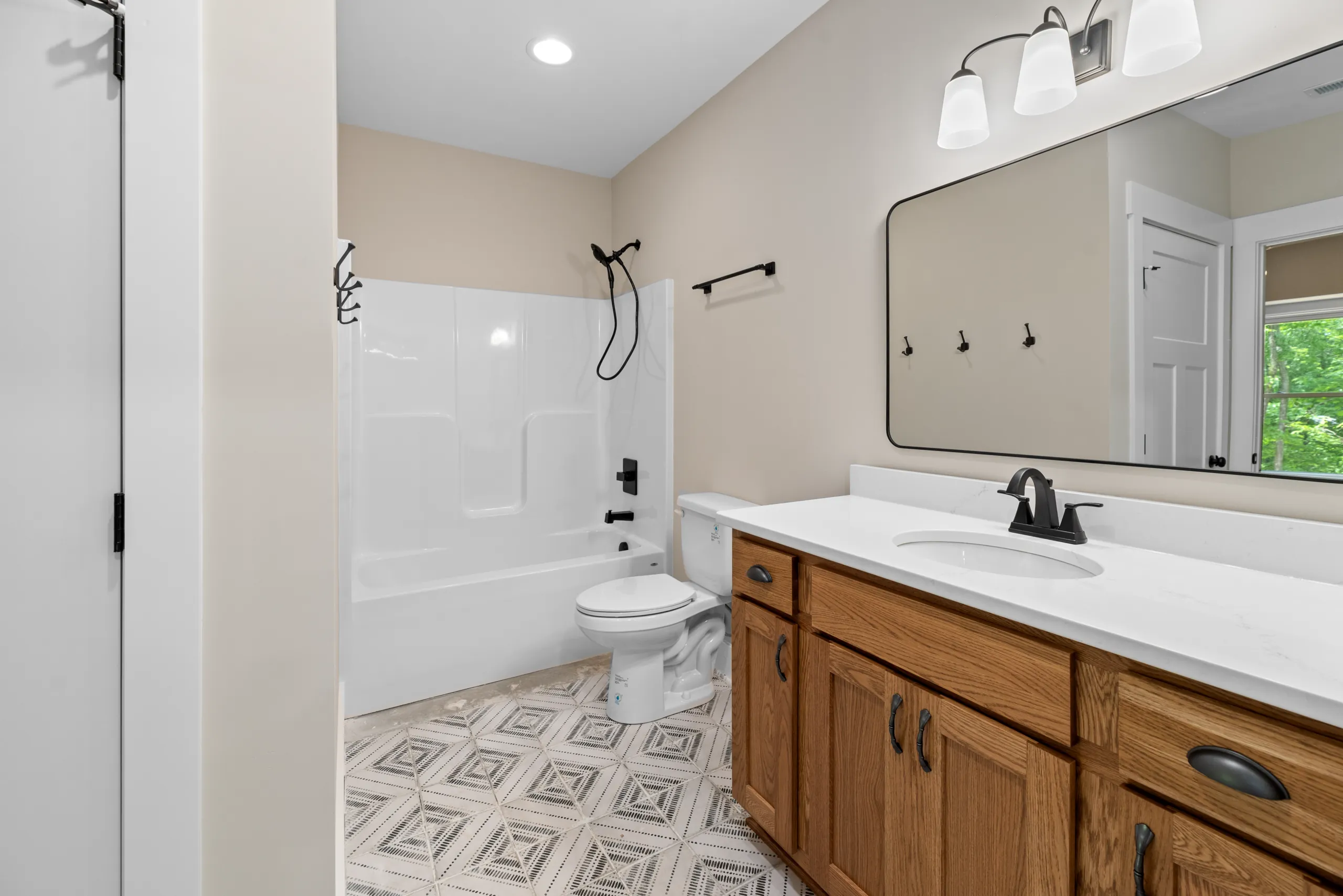 Bathroom with oak vanity, large black-framed mirror and tub-shower in the Lake Crest Home