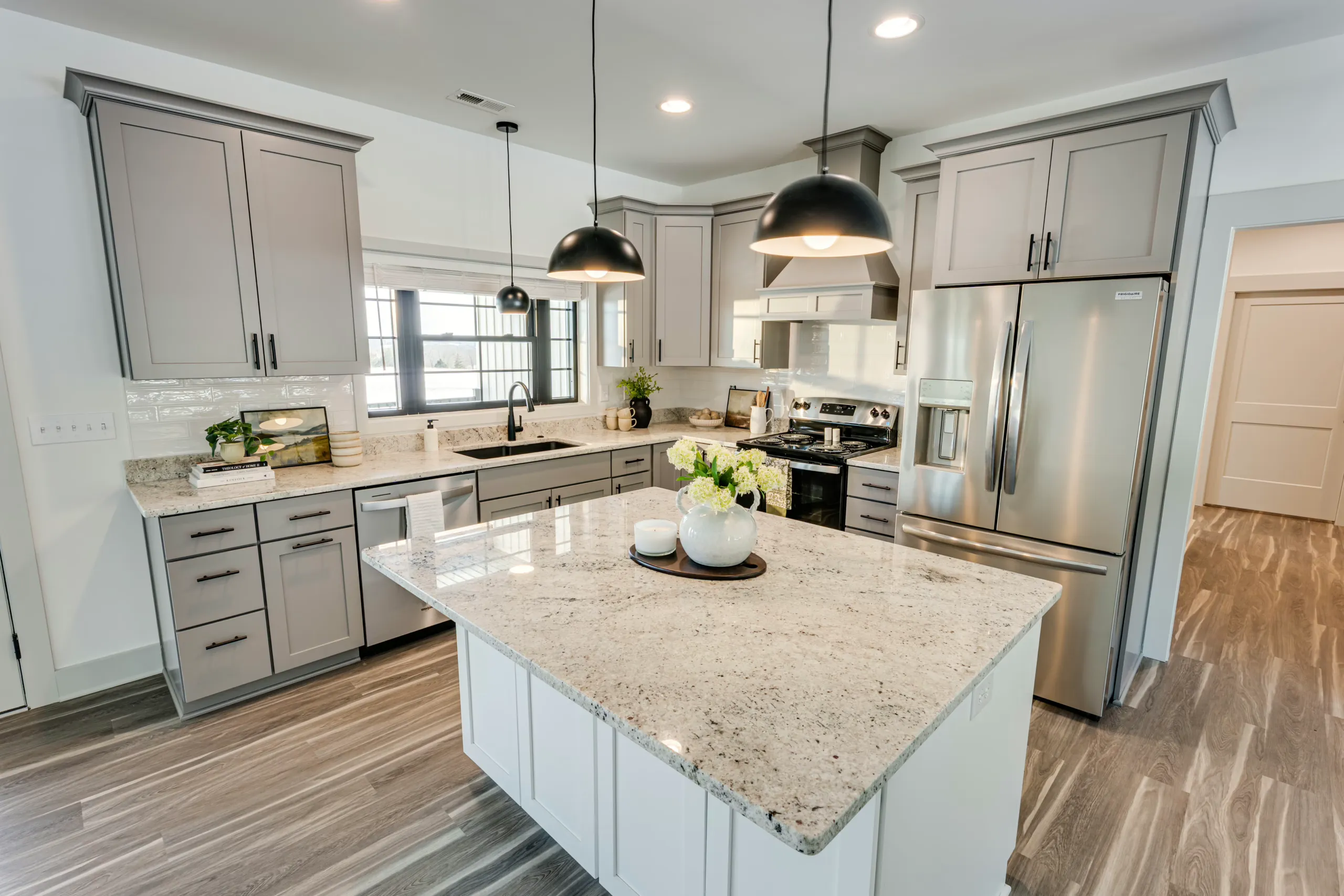 Kitchen with gray cabinets, granite island and black pendant lights in the Powell Lane Home