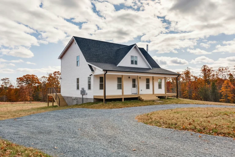 Exterior of the Meaders Mill Home, a white farmhouse with a covered front porch and gravel drive in autumn