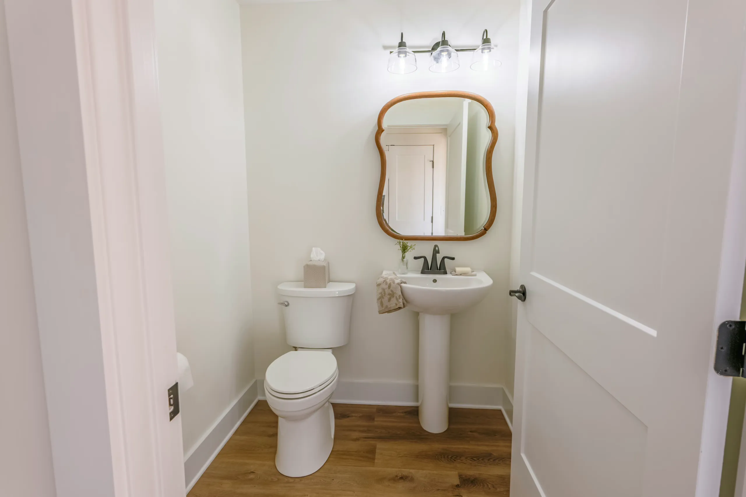 Half bath with pedestal sink and curved wood mirror in the Meaders Mill Home