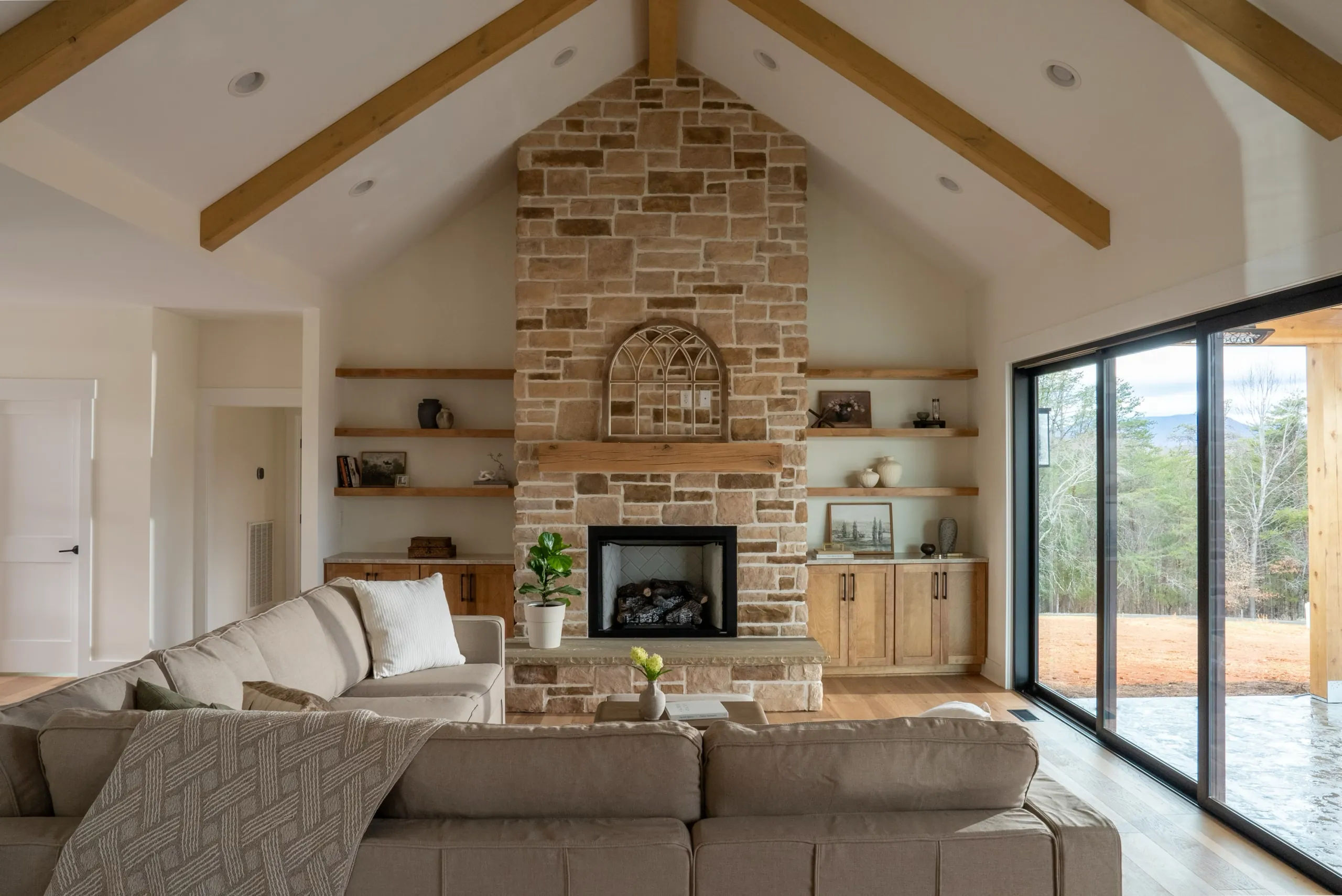 This warm inviting living room features accents of natural wood and manmade stone. Fireplace built-in's are on both sides of the earth-toned taupe veneer stone fireplace. The shelving for the built in's are made of a wood that compliments the custom wood cabinets beneath. The large sliding doors with black trim lead onto the patio adjacent to this room.