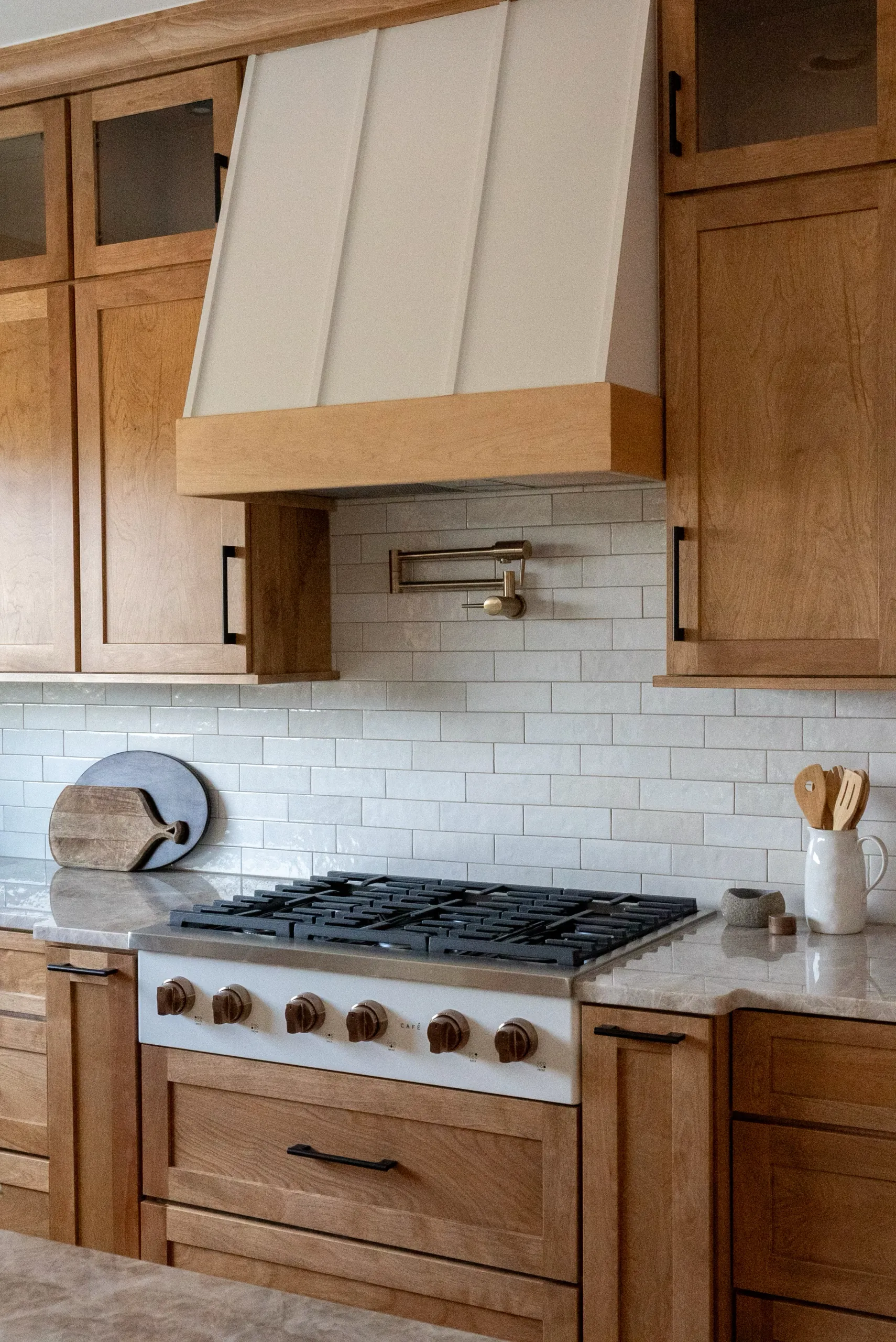 Magnolia Home kitchen range with wood cabinets, white vent hood and subway tile backsplash