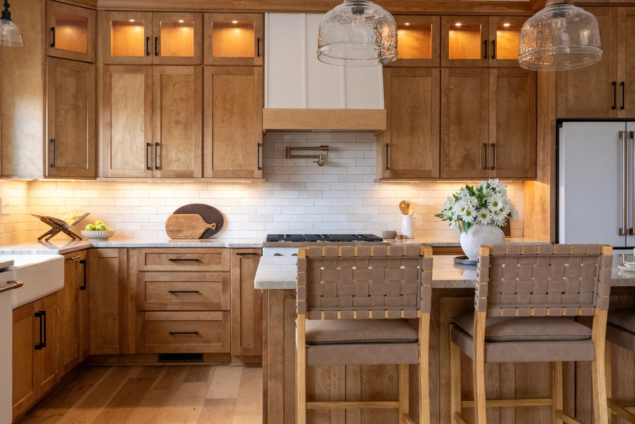 Magnolia Home kitchen with wood cabinets, glass pendants and an island with woven bar stools