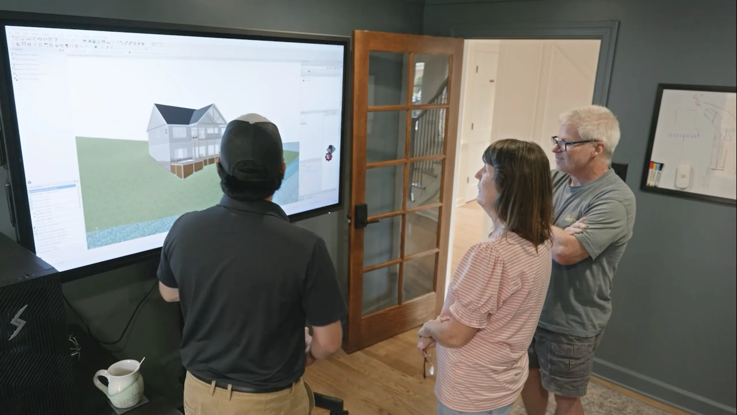 Sage Richardson showing clients a 3D rendering of their home design on an oversized, wall-mounted touch screen monitor.