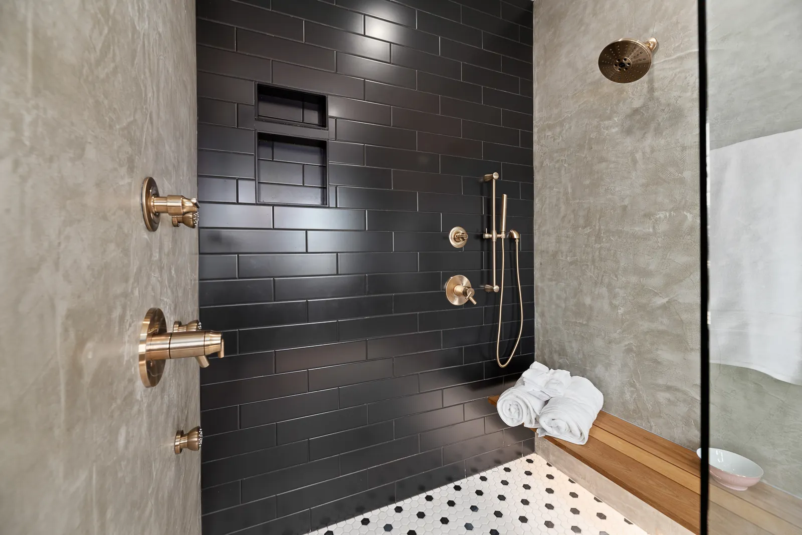Black tile shower with brass fixtures and teak bench in the Otter River Home