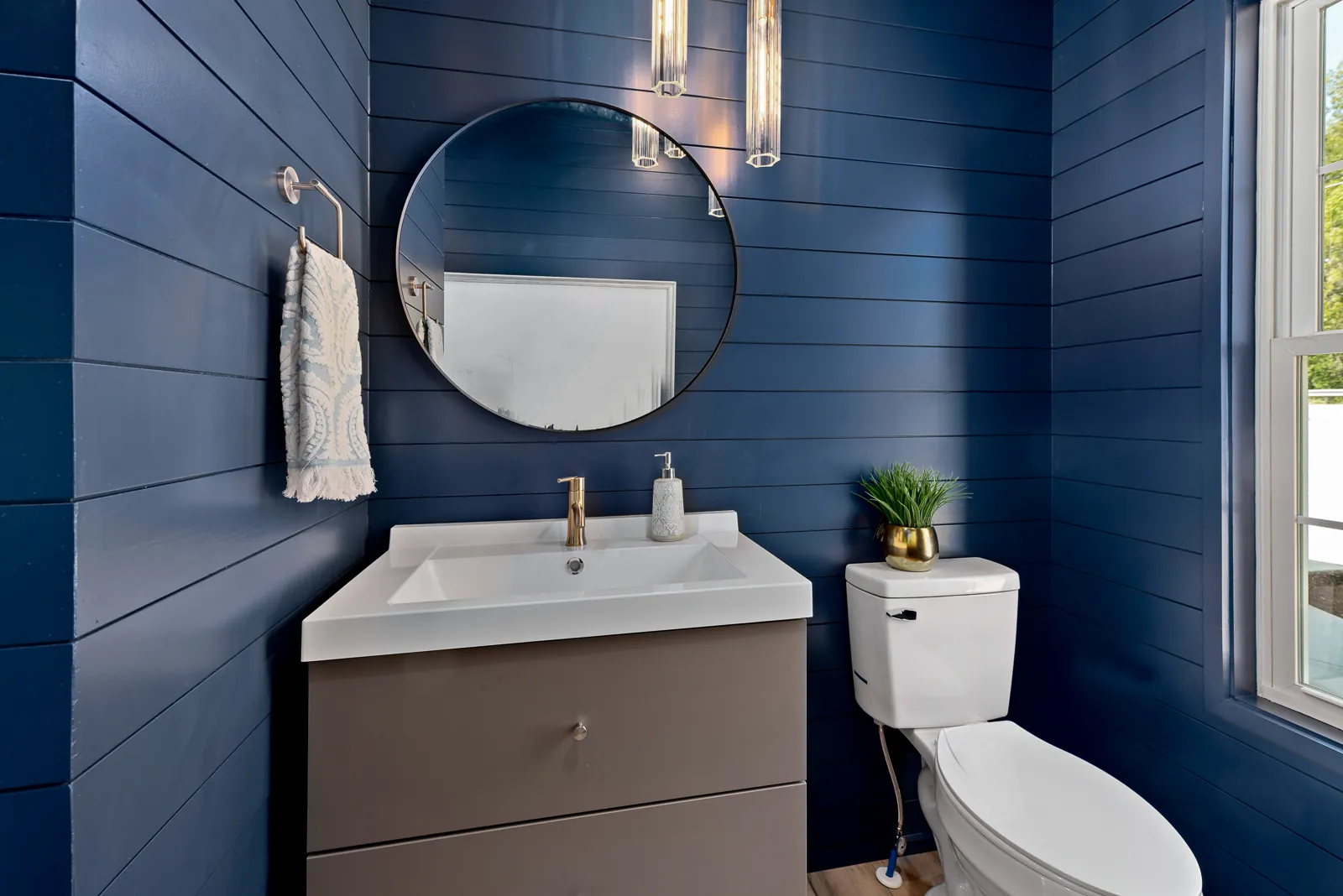 Powder room with navy shiplap walls and round mirror in the Otter River Home