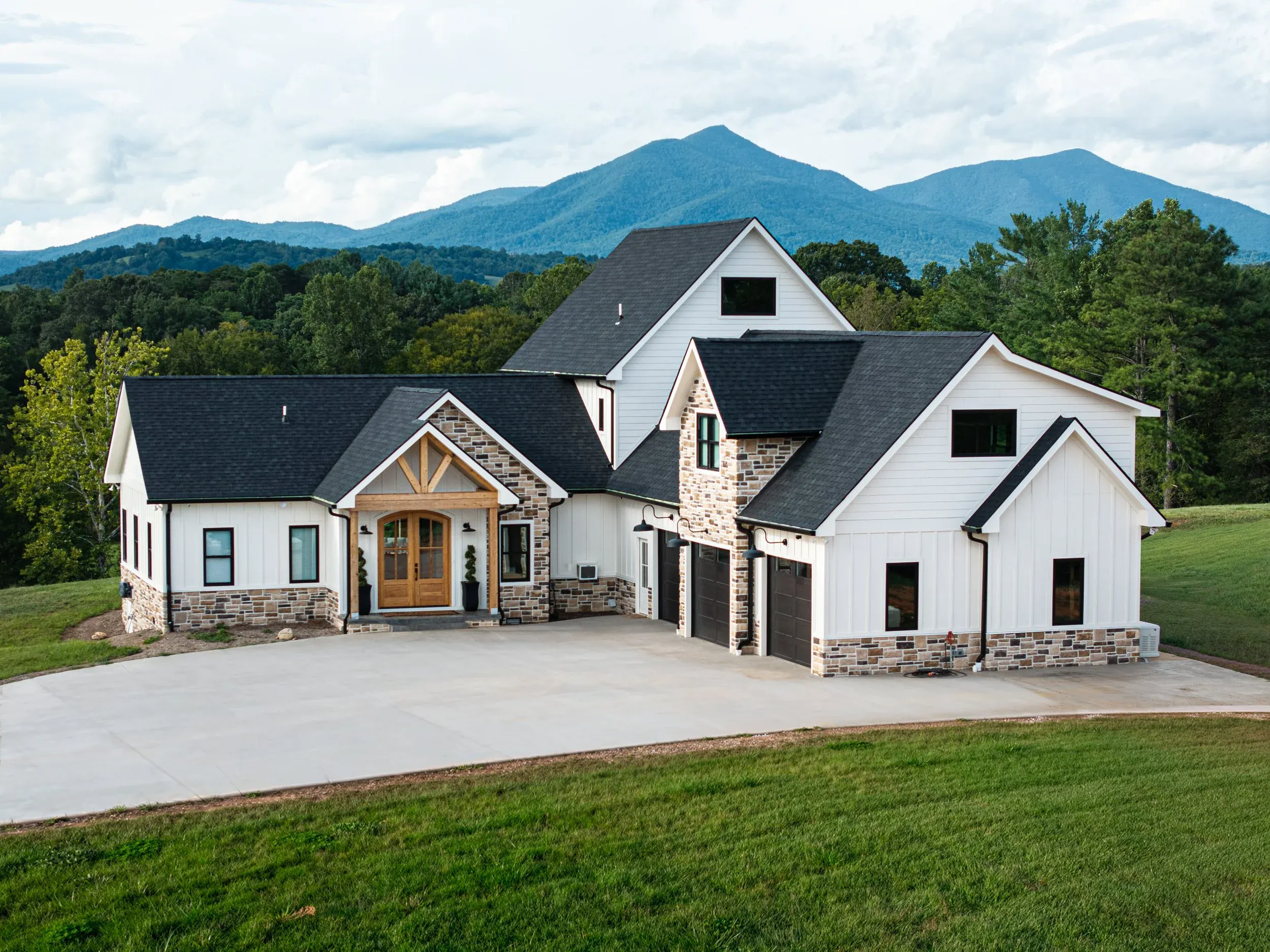 White farmhouse-style Magnolia Home with stone accents, timber entry and mountain backdrop