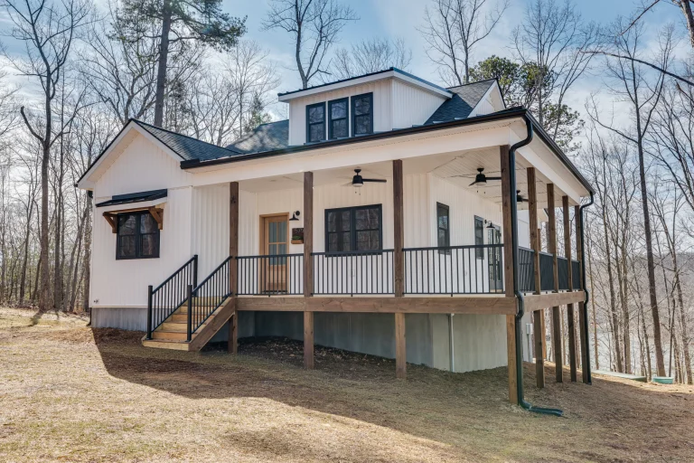 White farmhouse with a wraparound porch, black trim accents, and a natural wood craftsman-style front door.