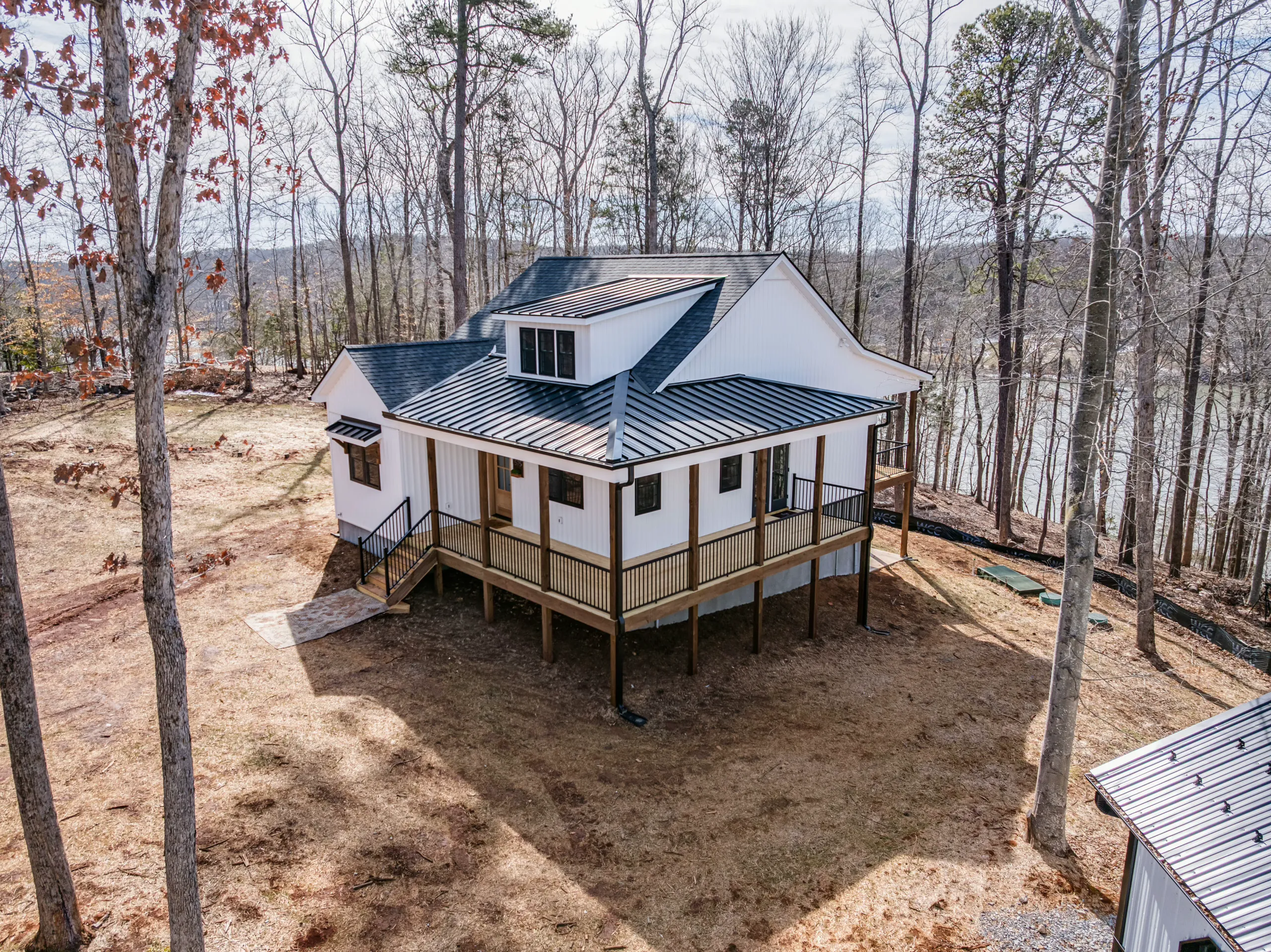 Aerial view of the Reservoir Home with metal porch roof in a wooded lot