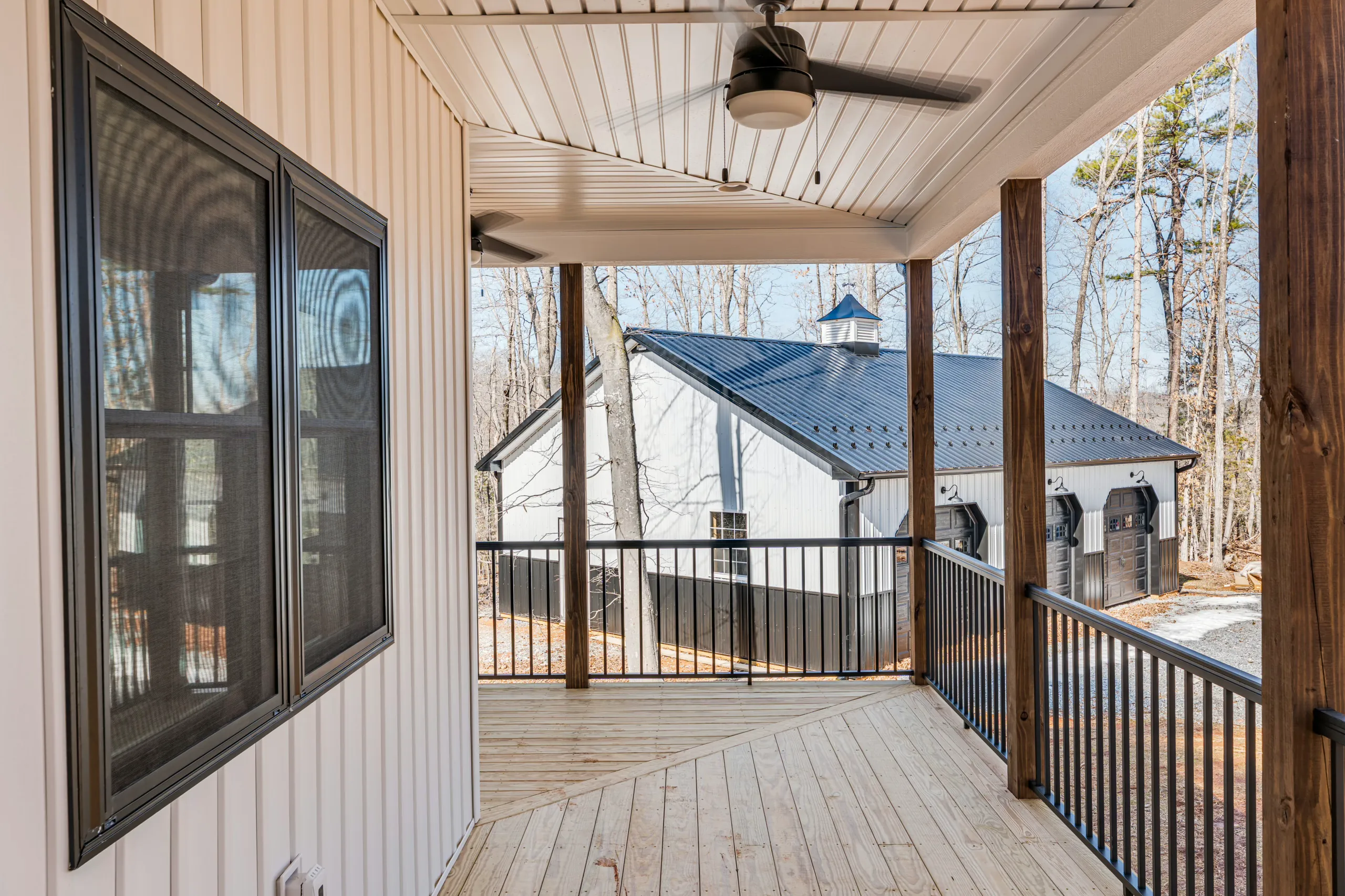 Front porch with ceiling fan, black railing and view of metal-roof outbuilding at the Reservoir Home