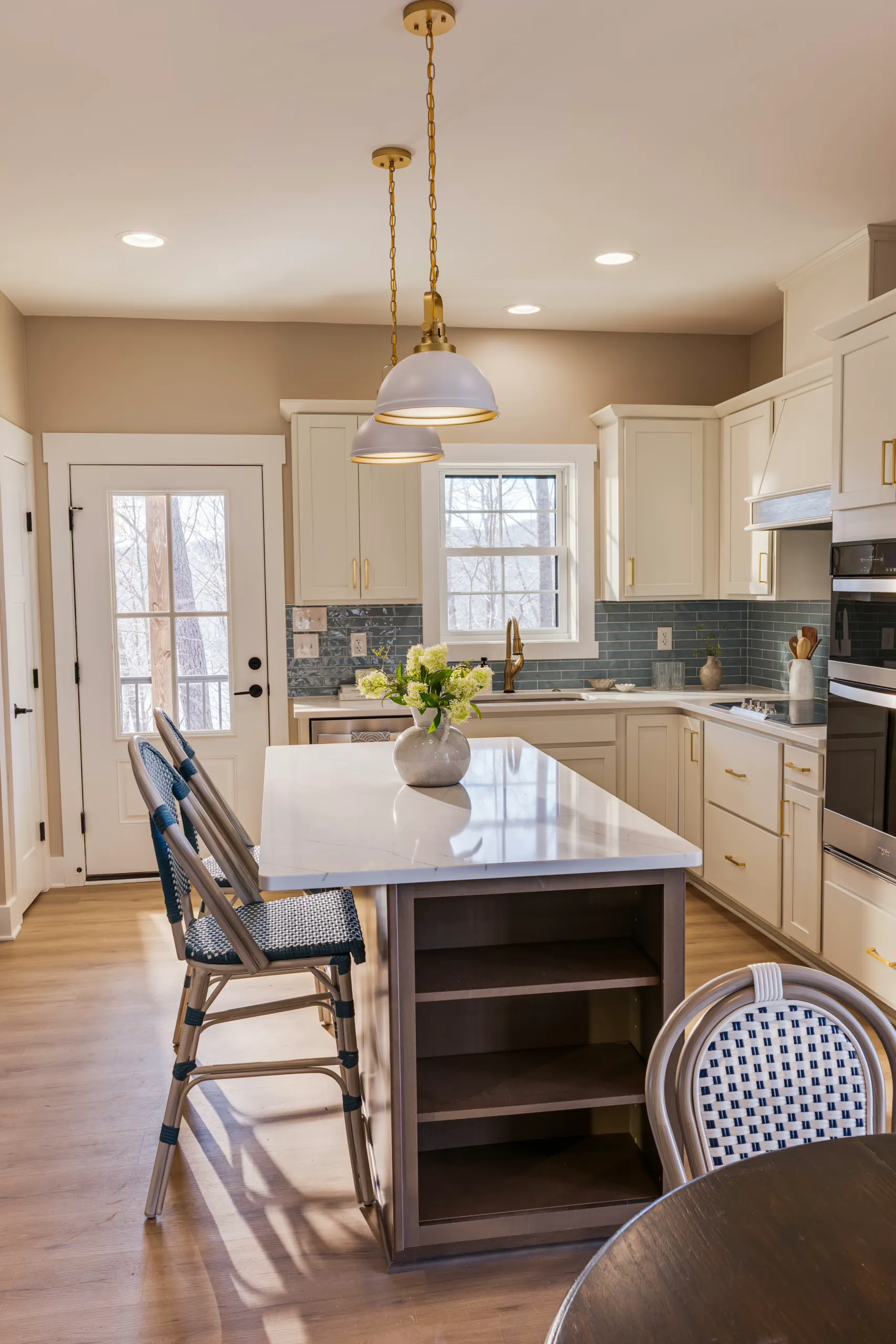 Kitchen with island, brass pendant lights and blue-gray tile backsplash in the Reservoir Home