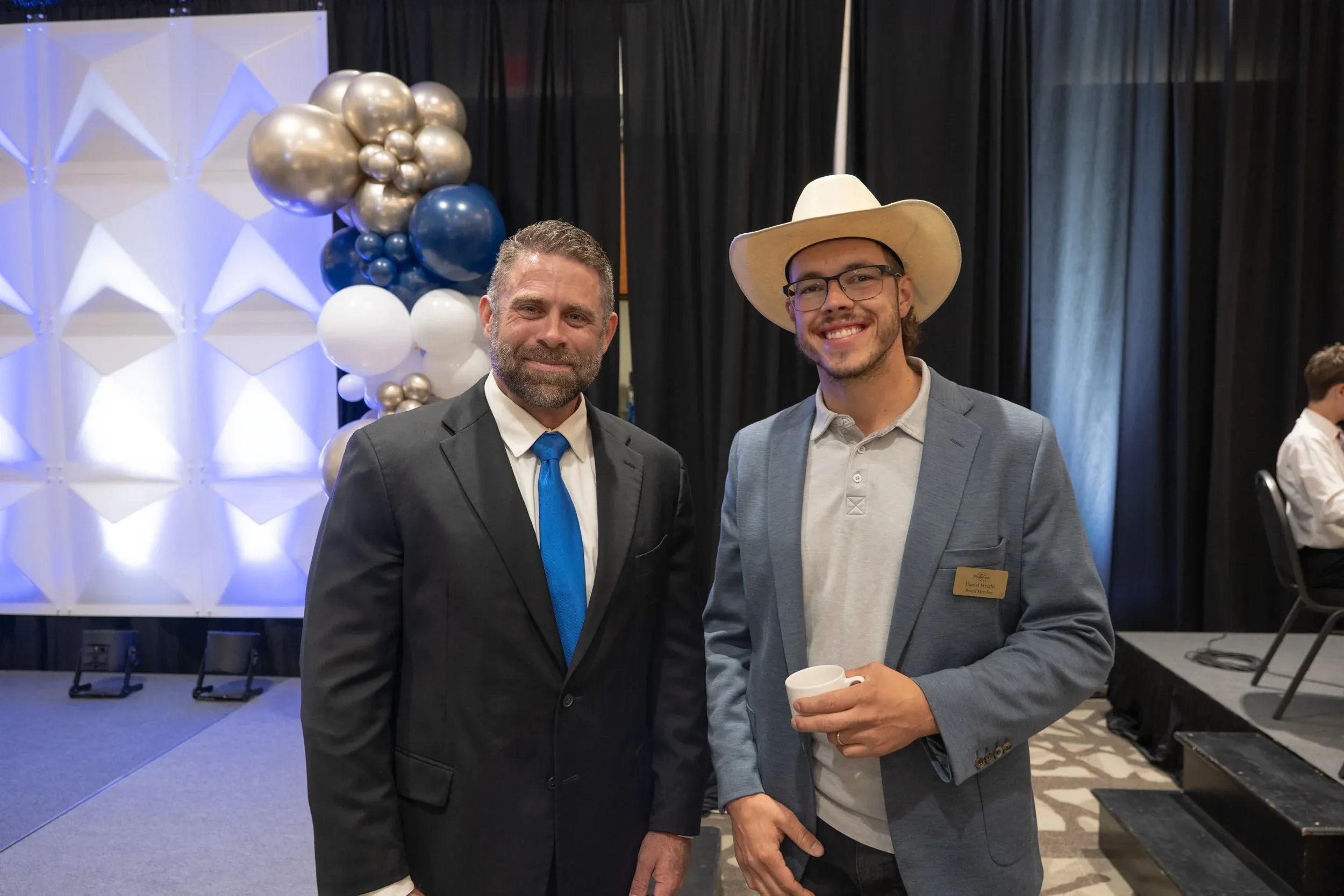 Two men smiling at an event in front of a balloon arrangement