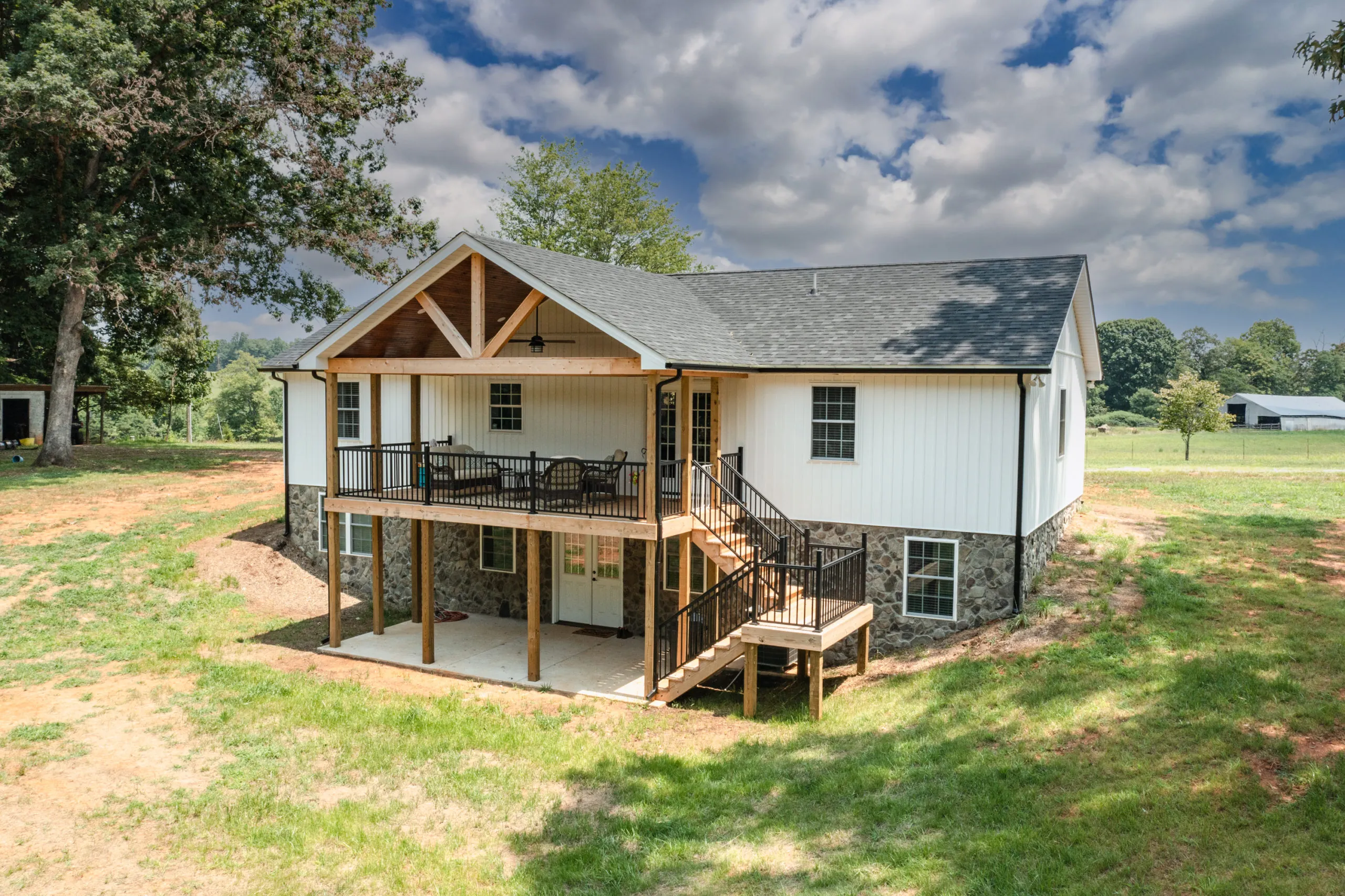 Rear of the Lake Cross Home with covered deck, stone foundation and walkout patio