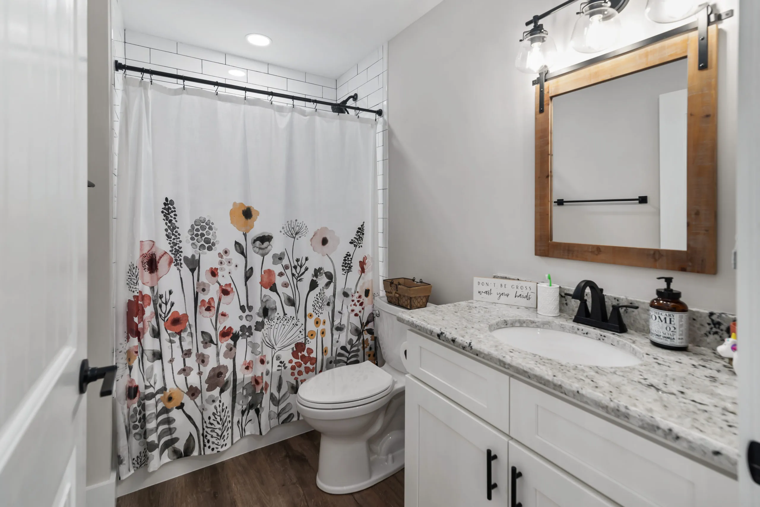 Bathroom with granite vanity, wood-framed mirror and floral shower curtain in the Lake Cross Home