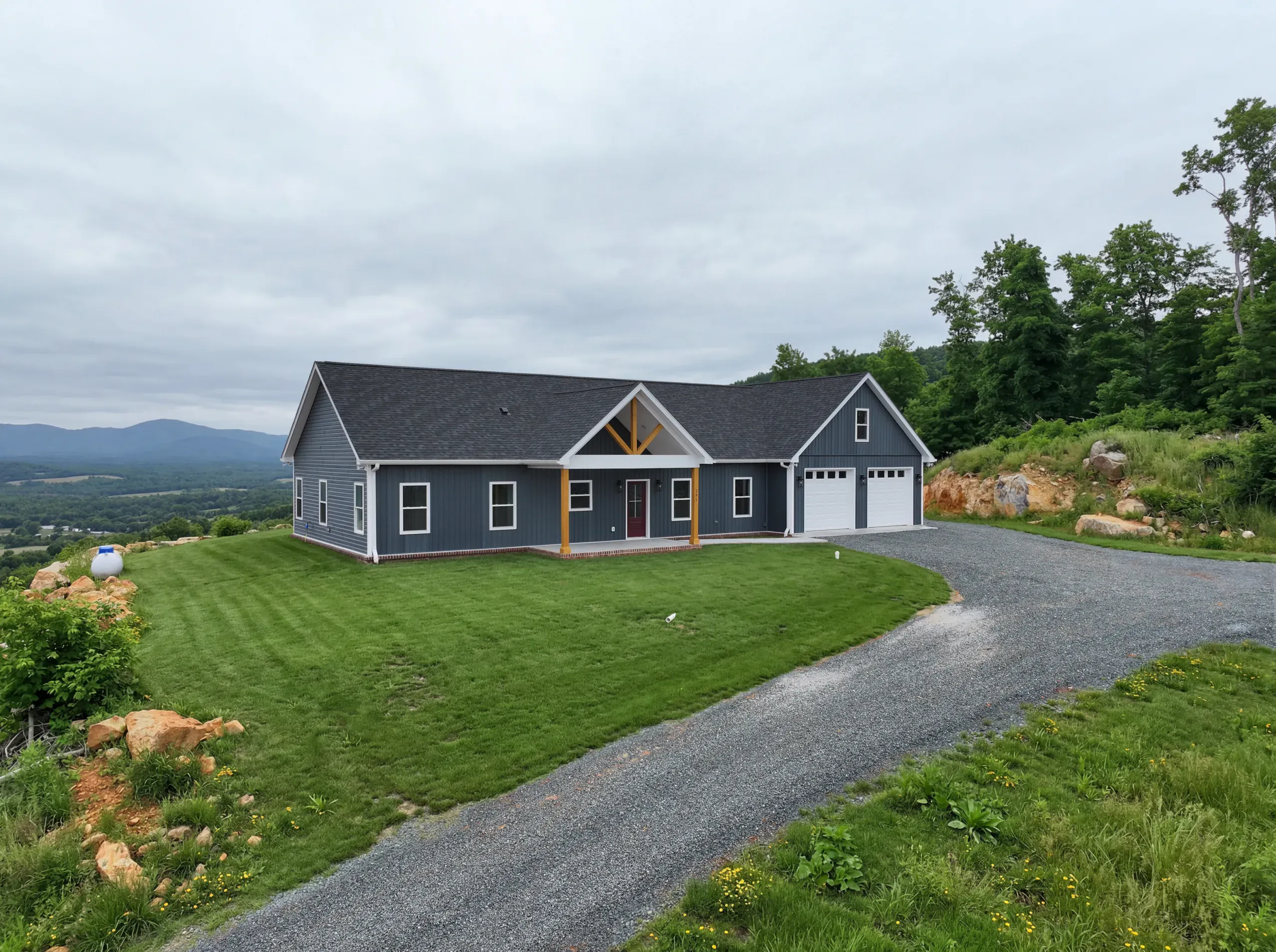 Front exterior of the Mountain Crest Home with blue siding, timber porch and two-car garage
