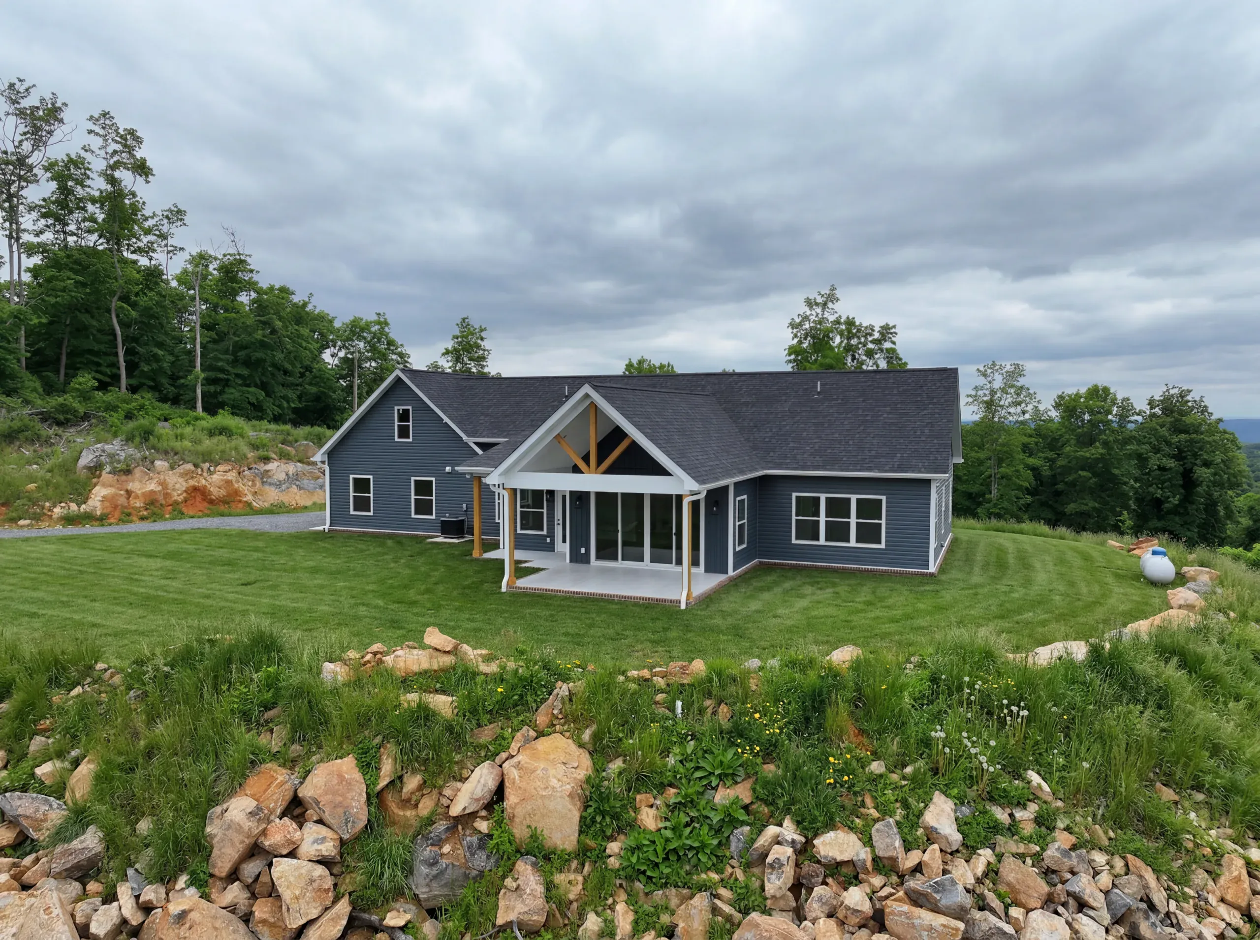 Rear covered porch and blue siding of the Mountain Crest Home on a hillside