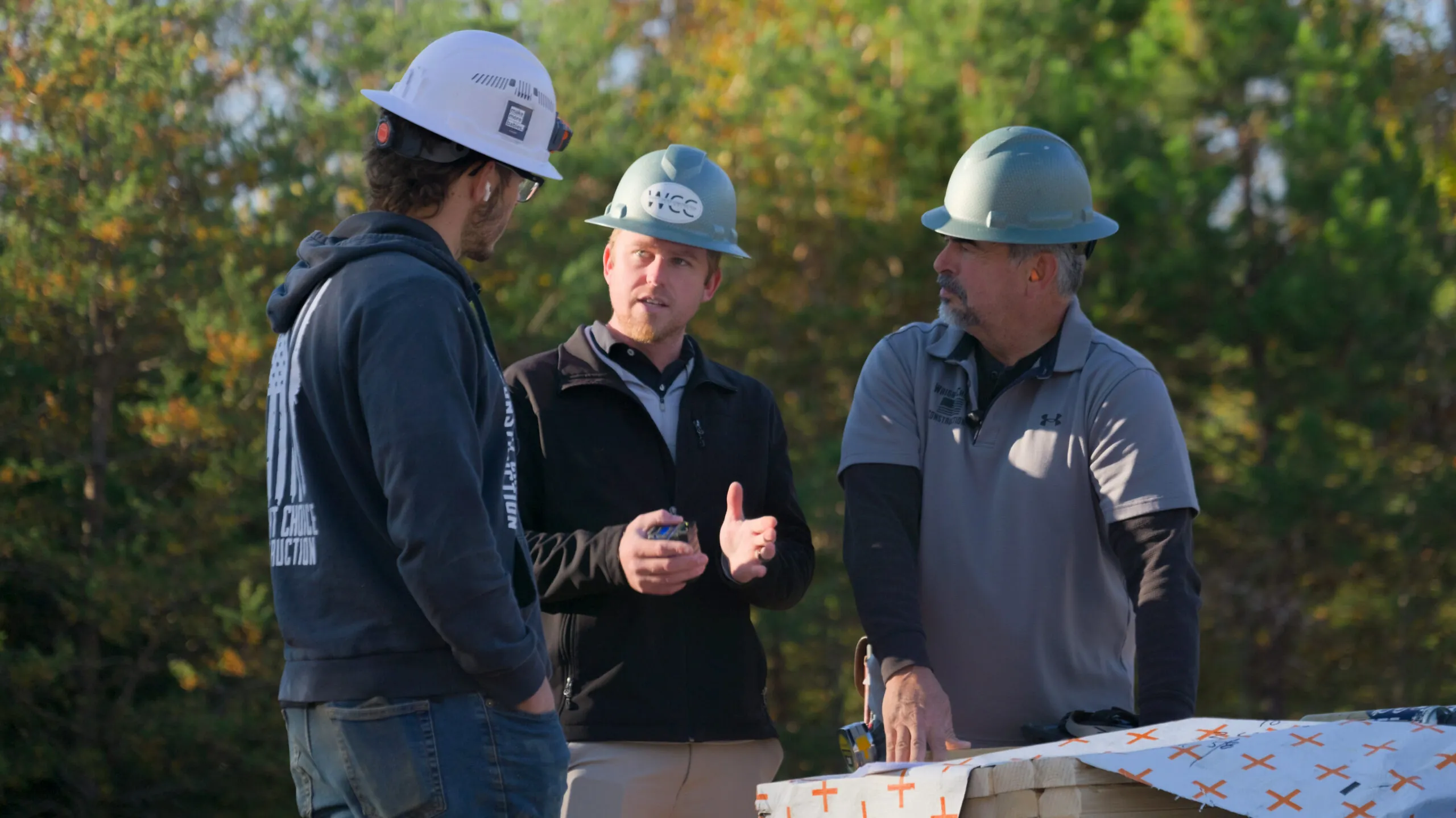 Project manager talking with two team members on the jobsite in hard hats